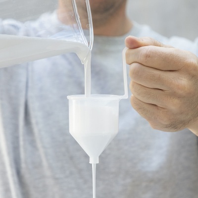 Pessoa a verter líquido branco num funil plástico transparente