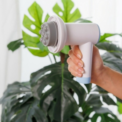 Aparelho portátil de massagem branco com detalhes azuis em frente a folhas verdes