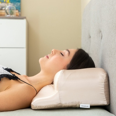 Almofada de apoio de tecido bege claro para pescoço numa cama com cabeceira cinza clara