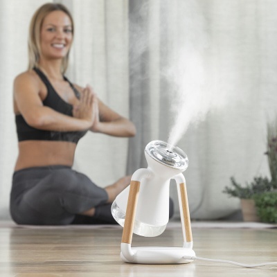 Humidificador branco com vapor, ao lado de pessoa em pose de ioga