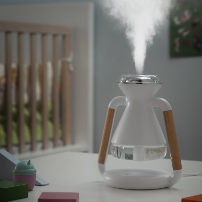 Humidificador branco com pernas de madeira a produzir vapor numa mesa com brinquedos ao redor