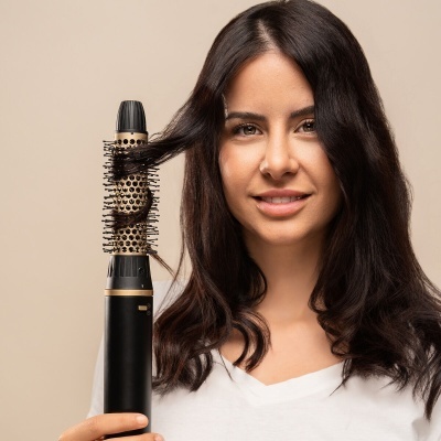 Mulher com cabelo castanho escuro segurando modelador de cabelo redondo dourado e preto com cabelo enrolado