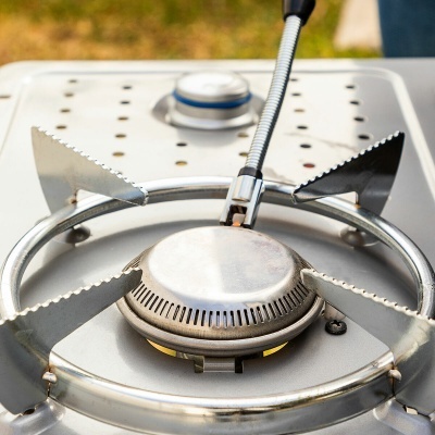Fogão portátil a gás prateado com queimador aceso e suportes dentados
