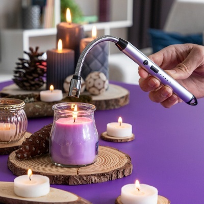 Isqueiro elétrico prateado acendendo vela roxa em frasco de vidro sobre base de madeira