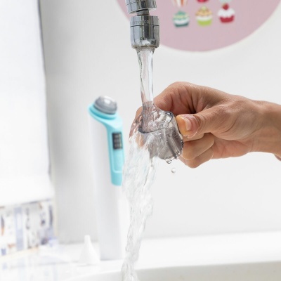 Mão limpando peça plástica transparente sob torneira com água corrente.