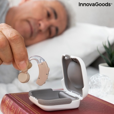 Dispositivo auditivo bege com caixa de carregamento branca ao lado do rosto de um idoso