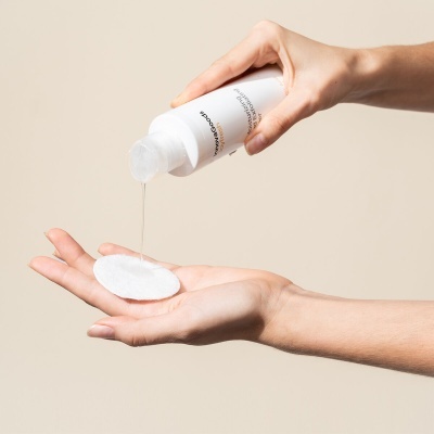 Frasco branco a verter líquido numa almofada de algodão