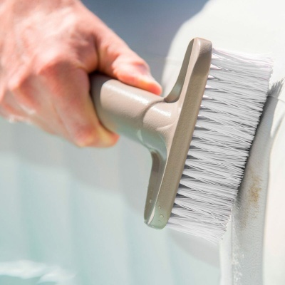 Escova manual cinzenta com cerdas brancas a limpar superfície branca