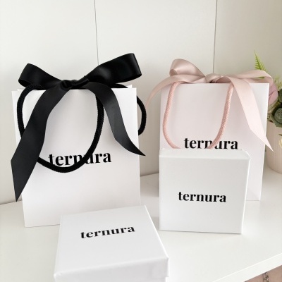 Sacos de papel e caixas brancas com 'ternura' e laços preto e rosa.