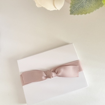 Caixa branca com fita rosa em laço sobre superfície branca e flores ao fundo