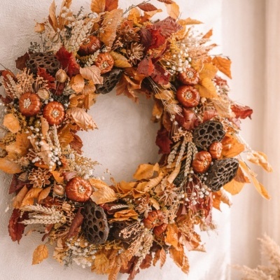 Grinalda decorativa de outono com folhas secas e pequenas abóboras laranja pendurada na parede