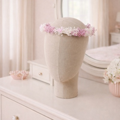 Diadema de flores rosa e branco em manequim de tecido numa cómoda branca com espelho e flores ao lado