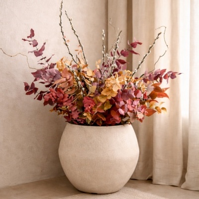 Jarro cerâmica branca com arranjo de folhas secas coloridas junto a cortina bege