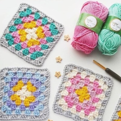Quadrados de croché coloridos, novelos de lã rosa e verde, botões de estrela e agulha de croché