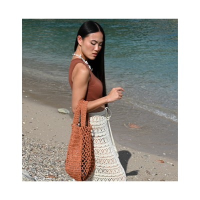 Mulher na praia com mala de crochet castanha e saia branca de crochet