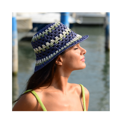 Mulher com chapéu de crochê azul, branco e verde perto de água
