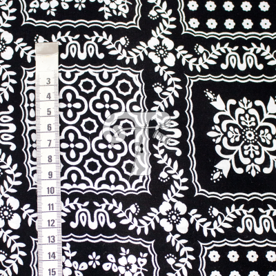 Tecido preto com padrão floral e geométrico em branco, fita métrica ao lado.