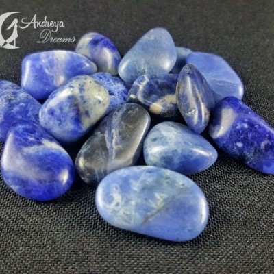 Pedras roladas azuis e brancas em superfície preta com logo Andreya Dreams