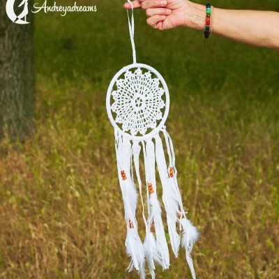 Apanha-sonhos branco decorativo com penas e contas, segurado à mão em ambiente natural