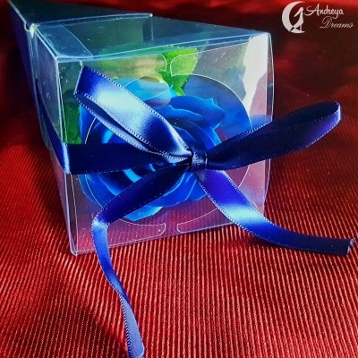 Caixa transparente com rosa azul artificial e fita azul sobre tecido vermelho