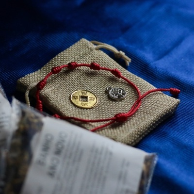 Pulseira fio vermelho, moedas dourada e prateada num saco de pano sobre tecido azul