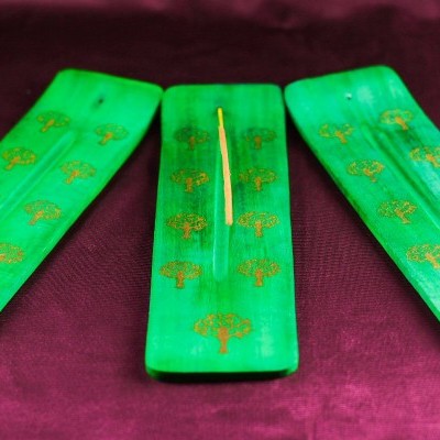 Três suportes verdes para incenso com desenhos dourados de árvores sobre tecido vermelho-escuro