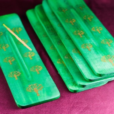 Suportes para incenso verdes em madeira com padrão dourado de árvores sobre tecido roxo