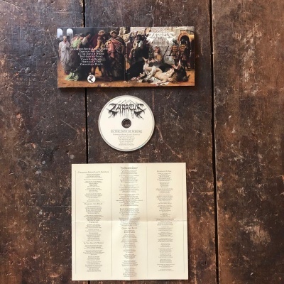 CD branco e capa com imagem de pessoas e leão sobre mesa de madeira com livreto com letras