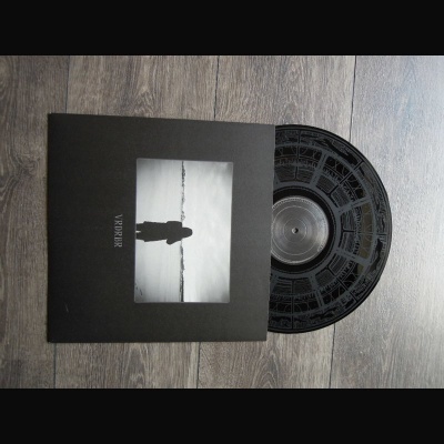 Disco de vinil preto com capa preta e imagem a preto e branco de silhueta junto a água sobre chão de madeira cinzenta