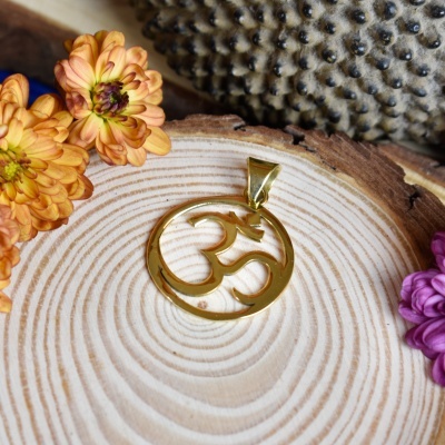 Pendente dourado com símbolo Om sobre madeira clara com flores coloridas