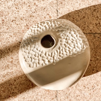 Vaso de cerâmica branco texturizado sobre chão de mosaico castanho claro