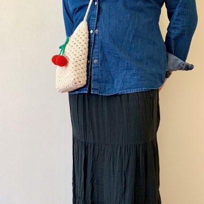 Bolsa em croché bege com pormenor vermelho e verde usada com camisa azul de ganga e saia preta.