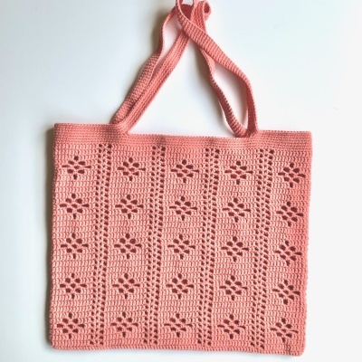 Saco de malha cor-de-rosa com padrão floral e duas alças sobre fundo branco.