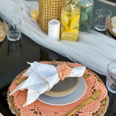 Mesa posta com decoração em tons naturais e detalhes em salmão, pratos e copos transparentes