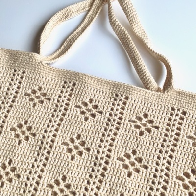 Saco de crochet bege com padrão de flores em relevo.