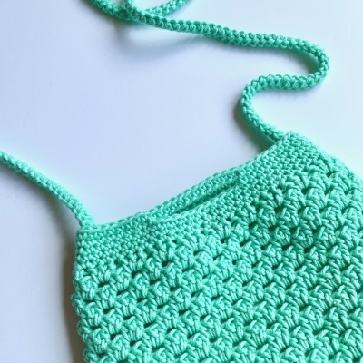 Top verde água de crochet com alças finas numa superfície branca