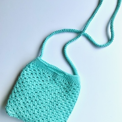 Bolsa azul clara de crochê com alça longa sobre fundo branco