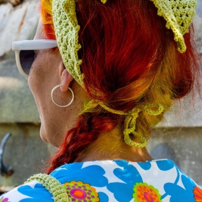 Pessoa com lenço verde claro em crochet e vestido azul com flores coloridas vista de costas