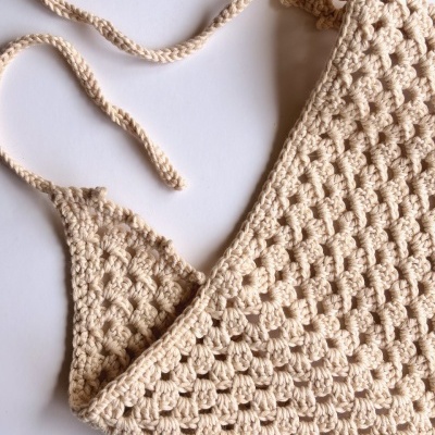 Top de crochet bege com padrão texturizado e alças trançadas sobre fundo branco