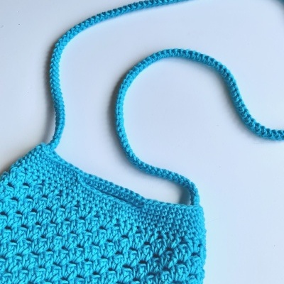 Bolsa azul de crochet com alça fina sobre superfície branca
