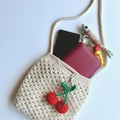 Mala de croché bege com cerejas vermelhas e itens dentro