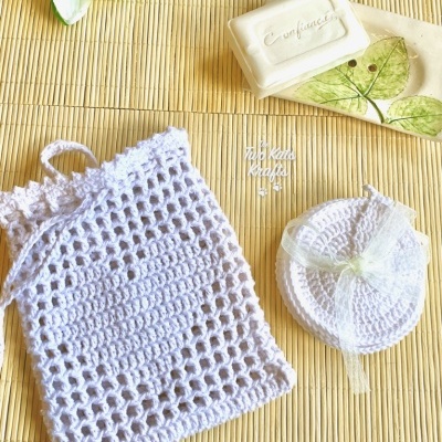 Dois sacos de crochê brancos e saboneteira com sabonete em fundo de palha clara