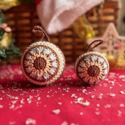 Ornamentos redondos de croché castanhos, creme e azul, sobre tecido vermelho com flocos brancos.