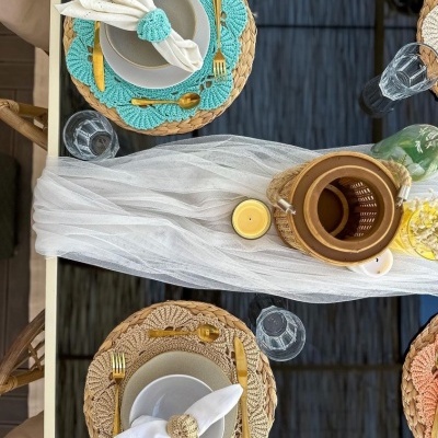 Mesa posta com pratos brancos, bases redondas coloridas, talheres dourados e guardanapos brancos com argolas de tecido.