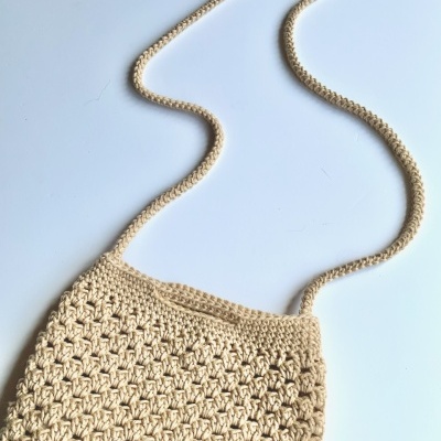 Bolsa de croché bege com alça sobre fundo branco