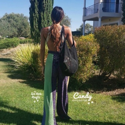 Mulher com calças largas coloridas, top preto e mala preta numa zona ajardinada