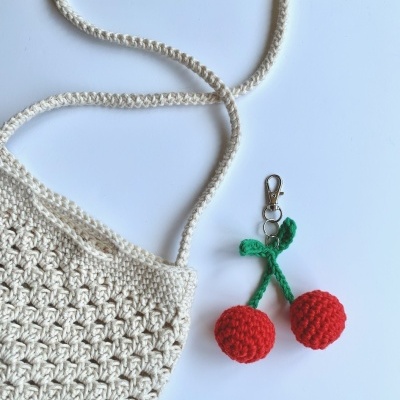 Bolsa de crochê bege com cordão e porta-chaves de cerejas de crochê