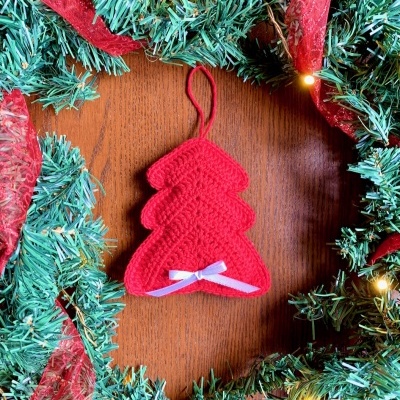 Enfeite de árvore de Natal vermelho em crochê com fita branca, guirlanda verde e luzes amarelas.