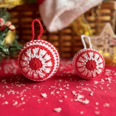 Bolas de Natal de croché vermelho e branco sobre tecido vermelho com flocos artificiais.