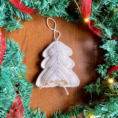 Ornamento de Natal em forma de árvore branca tricotada pendurado em guirlanda verde com fita vermelha e luzes